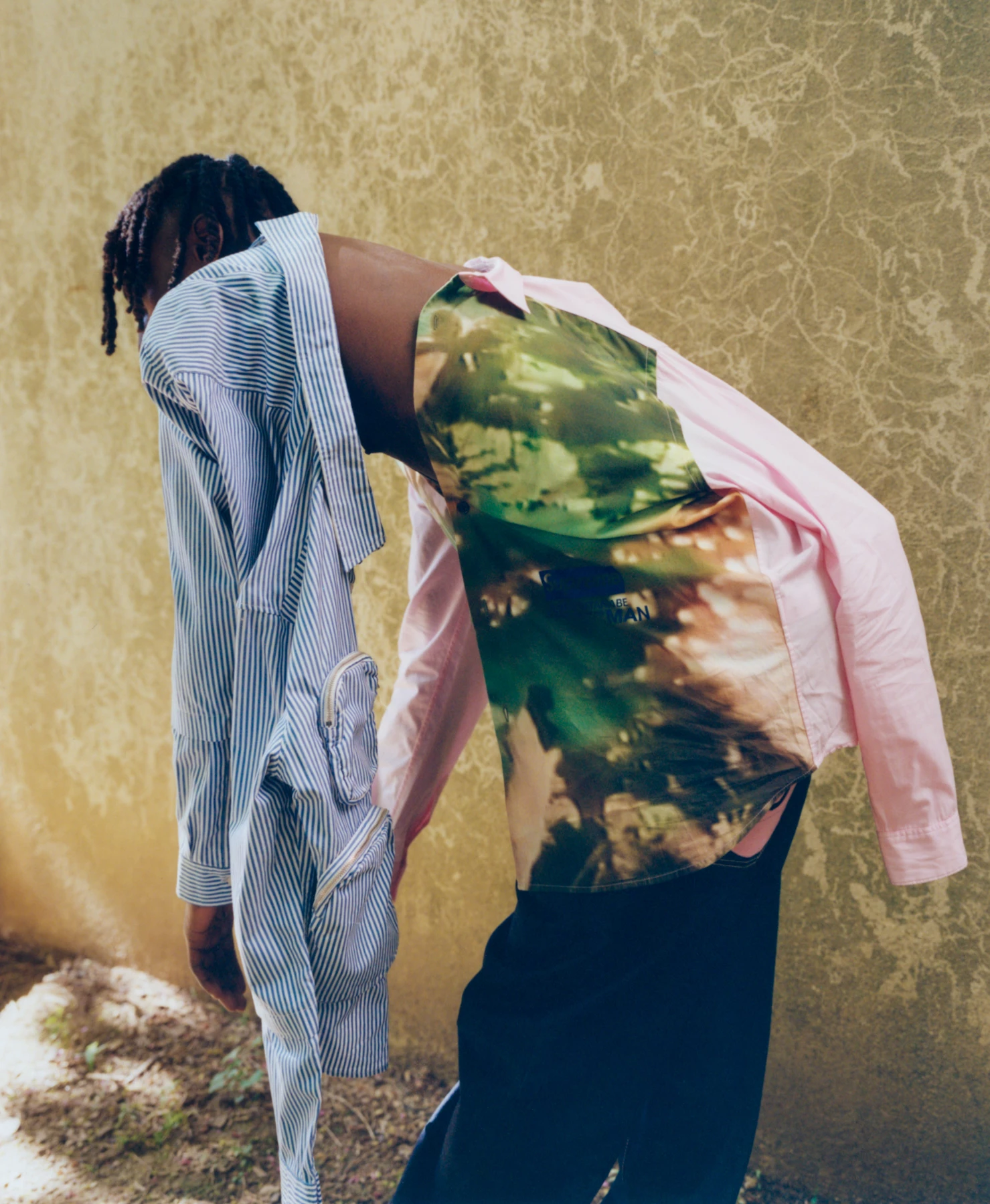 Le photographe de mode appelé Raul Guillermo a photographié ce visuel. Ce visuel présente un mannequin en mouvement portant plusieurs chemises en même temps. Une des chemises est bleue à rayures, l’autre rose et dans des tons verts de camouflage. La photographie est photographiée en extérieur derrière un mur marbré de couleur beige / jaune et avec des nuances de vert.