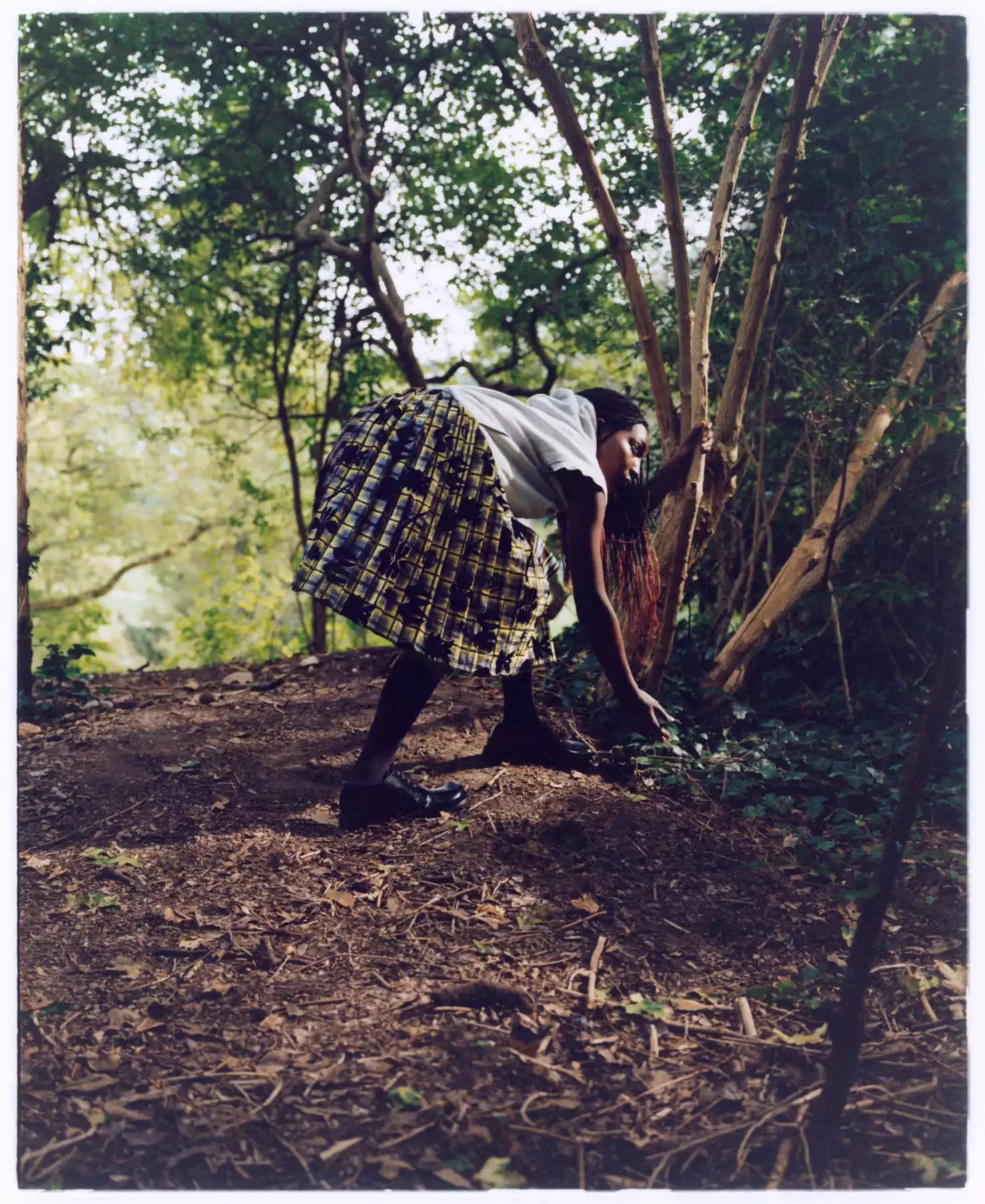Cette photographie est l’oeuvre du photographe de mode Raul Guillermo. Nous y voyons une jeune mannequin habillée d’une jupe à carreaux dans les tons de vert et de jaune. La mannequin se penche pour rammaser quelque chose au sol. La photographie a été réalisée dans une forêt. L’auteur, le photographe Raul Guillermo aime le travail des couleurs fortes. Il aime aussi photographier à l’argentique.