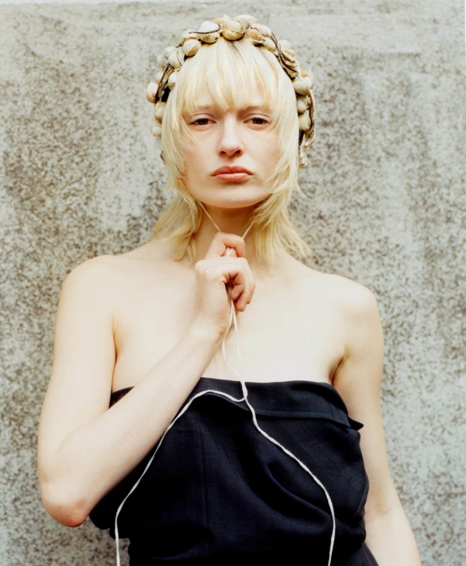 Le photographe Raul Guillermo a photographié ce portrait d’une mannequin blonde. La mannequin blonde est photographié sur un mur, en extérieur. La mannequin porte une robe noire et un serre-tête. Elle nous regarde d’un regard assuré. Le photographe Raul Guillermo est une photographe de mode qui photographie tant à l’argentique qu’au numérique. L’agent du photographe Raul Guillermo est Alexis Antigny, le créateur de l’agence ANTIGNY AGENCY