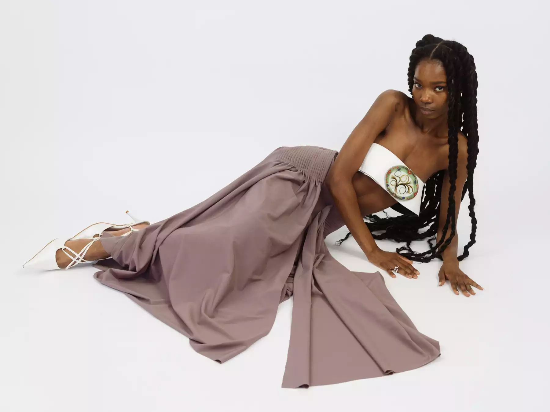 Cette photographie nous montre le portrait d’une jeune femme allongé sur un fond blanc. La mannequin porte une longue jupe de couleur marron, un bustier blanc et des chaussures blances. l’attitude du mannequin est assurée. L’auteur de cette photographie est le photographe de mode Raul Guillermo. Le photographe est représenté par l’agence de photographes appelée ANTIGNY AGENCY.