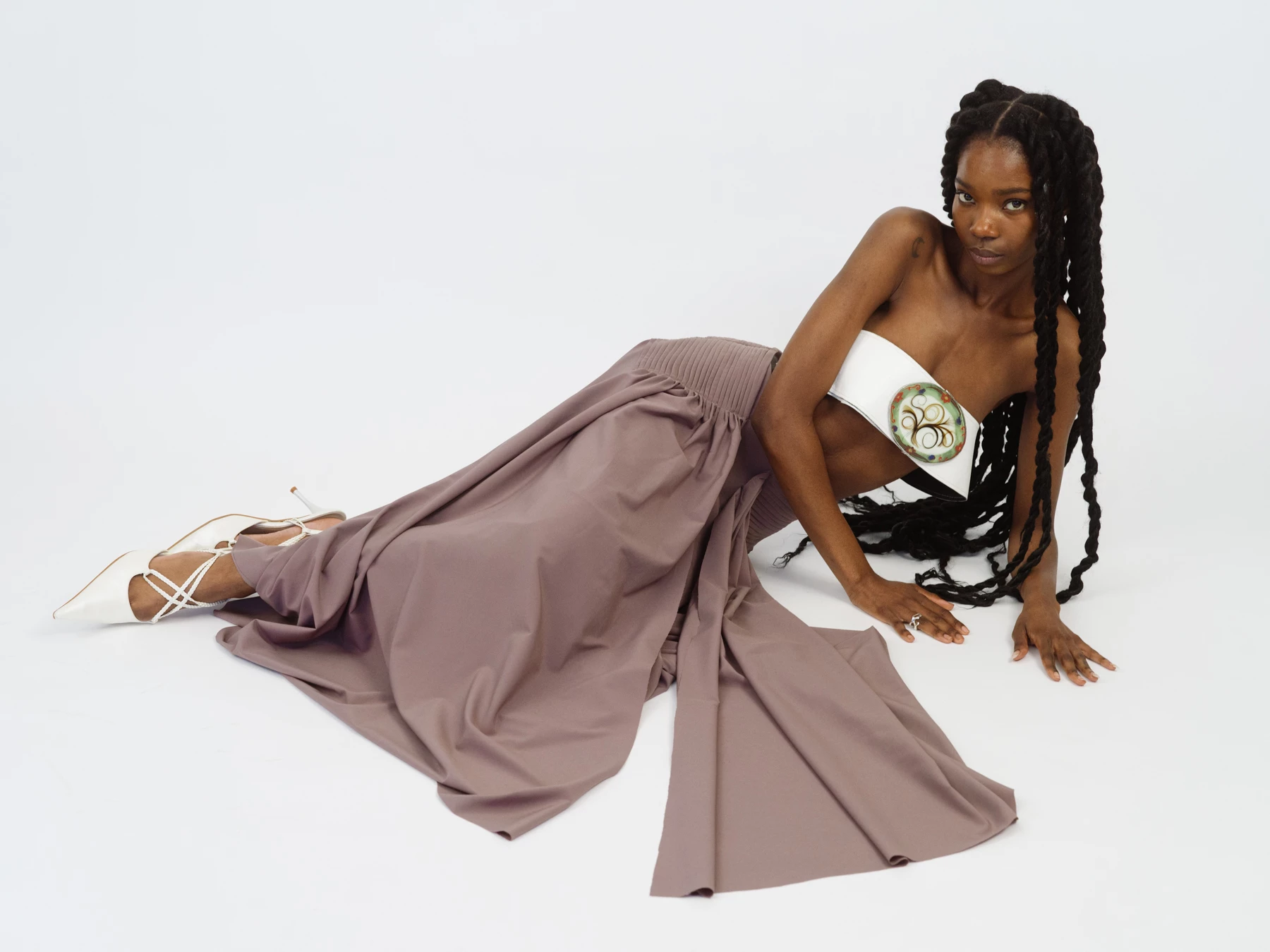 Cette photographie nous montre le portrait d’une jeune femme allongé sur un fond blanc. La mannequin porte une longue jupe de couleur marron, un bustier blanc et des chaussures blances. l’attitude du mannequin est assurée. L’auteur de cette photographie est le photographe de mode Raul Guillermo. Le photographe est représenté par l’agence de photographes appelée ANTIGNY AGENCY.