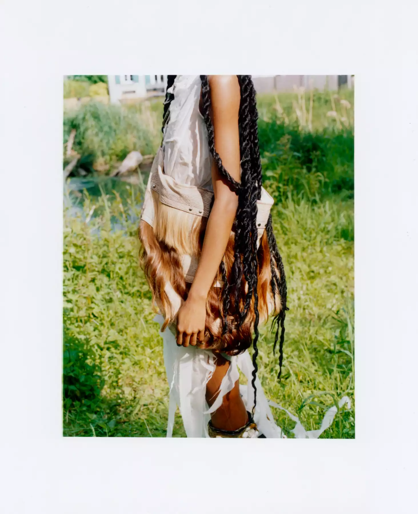 Le photographe de mode est l’auteur de ce gros plan du buste de cette mannequin. Le cadre serré ne nous permet pas de voir le visage de la mannequin. La mannequin porte une robe blance et un sac dans les tons de marrons. La photographie est une photographie argentique. Le procédé de la photographie argentique est une des techniques photographiques du photographe de mode Raul Guillermo. La scène se situe en extérieur, probablement près d’une rivière.